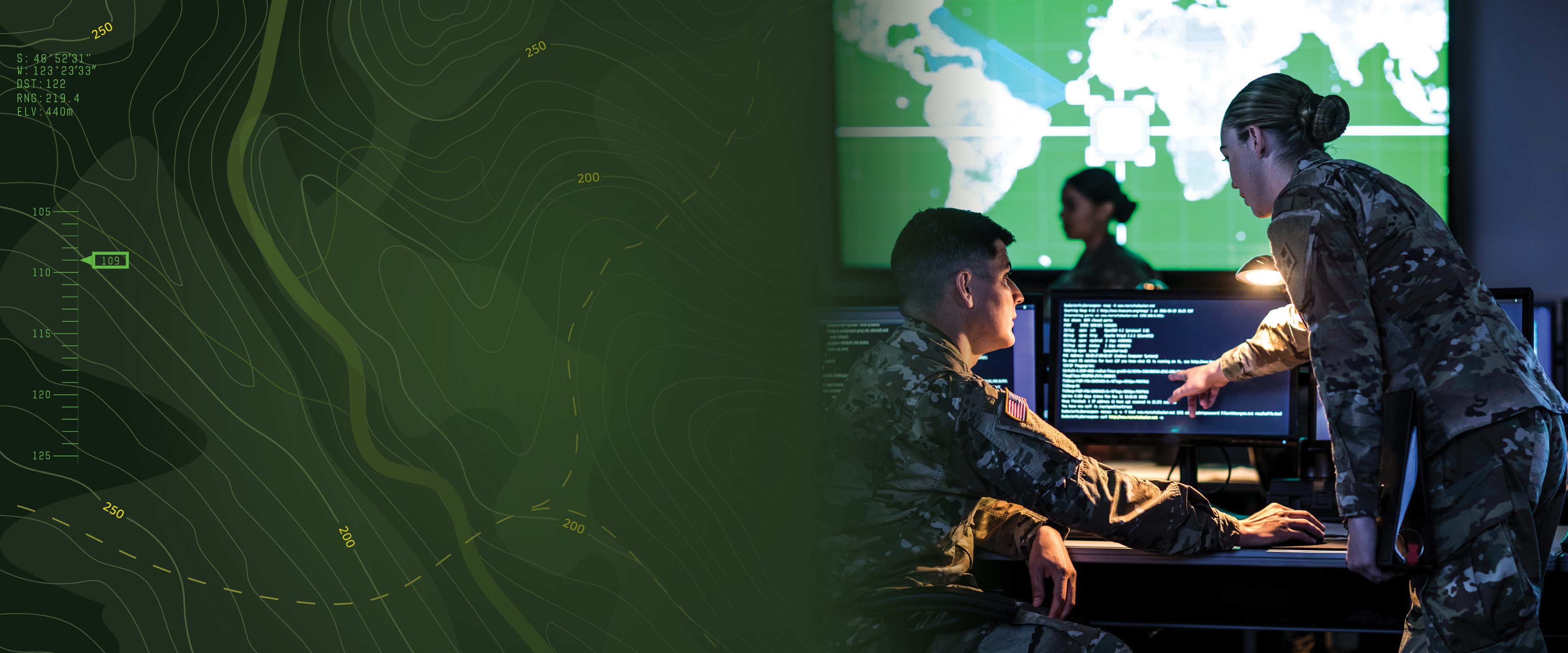 Two soldiers in uniform point at a computer screen with a U.S. map on a large screen in the background.
